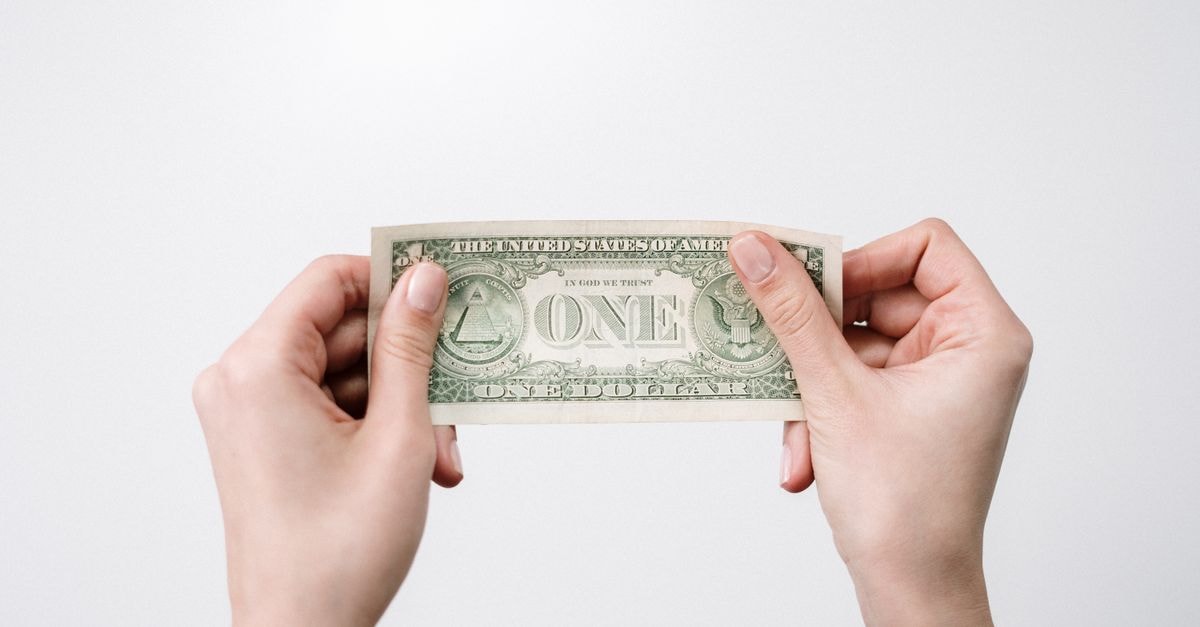 A close-up image of hands holding a one dollar bill, symbolizing finance and economy.
