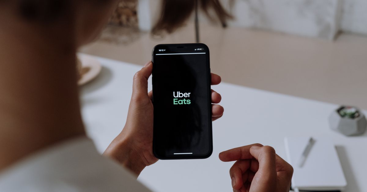 Waymo to Launch Own App in Austin and Atlanta, Ending Exclusive Uber Robotaxi Deal Person holding a smartphone using Uber Eats. Indoor setting with a clear view of the app interface.
