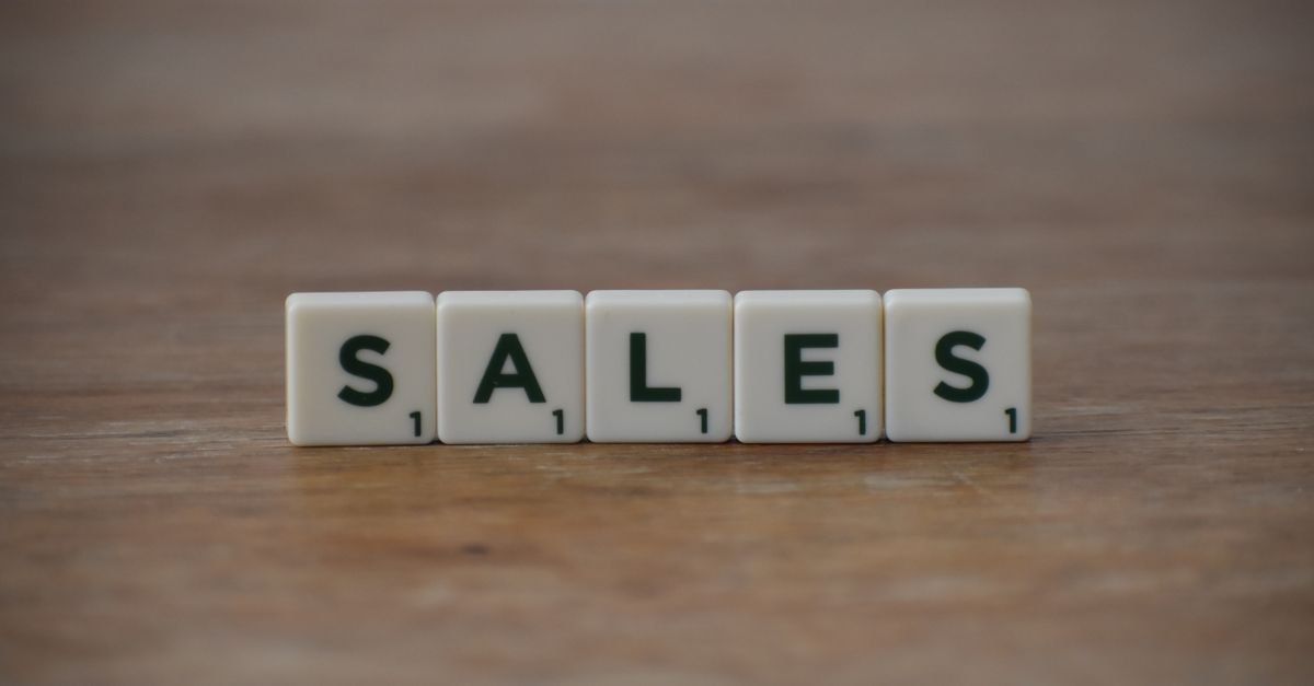 木桌上拼字遊戲字母塊拼出「sales」（銷售）一字，強調商業與行銷主題。