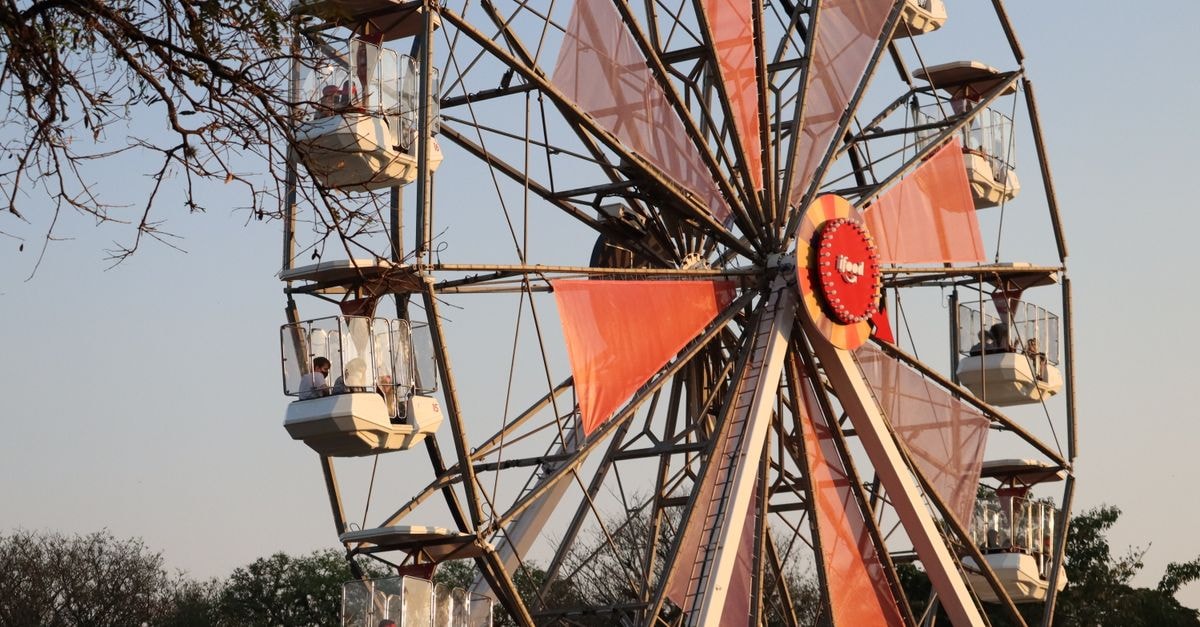Vibrant Ferris wheel spinning at sunset among trees, capturing a joyful atmosphere in SP, Brazil.