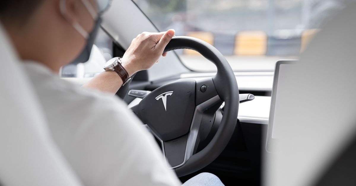 Zoox Wins First U.S. Robotaxi Exemption as Tesla's Paid Autonomous Miles Slide Close-up photo of a person driving a Tesla, showcasing modern vehicle interior design.