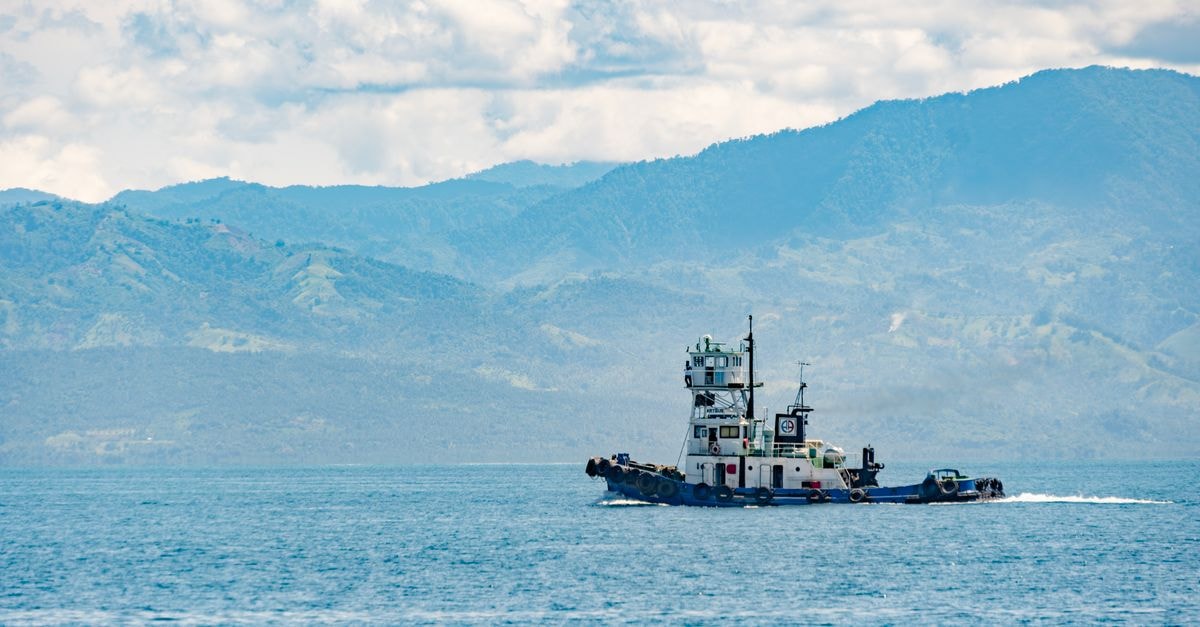 General Santos City Travel Guide: Tuna Country Beyond the Buzz Tugboat navigating Sarangani Bay with expansive mountain backdrop under bright skies.