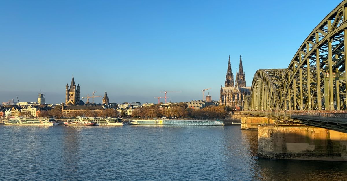 Hotel Zum Kostbaren Blut in Cologne: Altstadt-Nord Address Near Old Town Sights Scenic view of Cologne's iconic cathedral and Hohenzollern Bridge over the Rhine River.