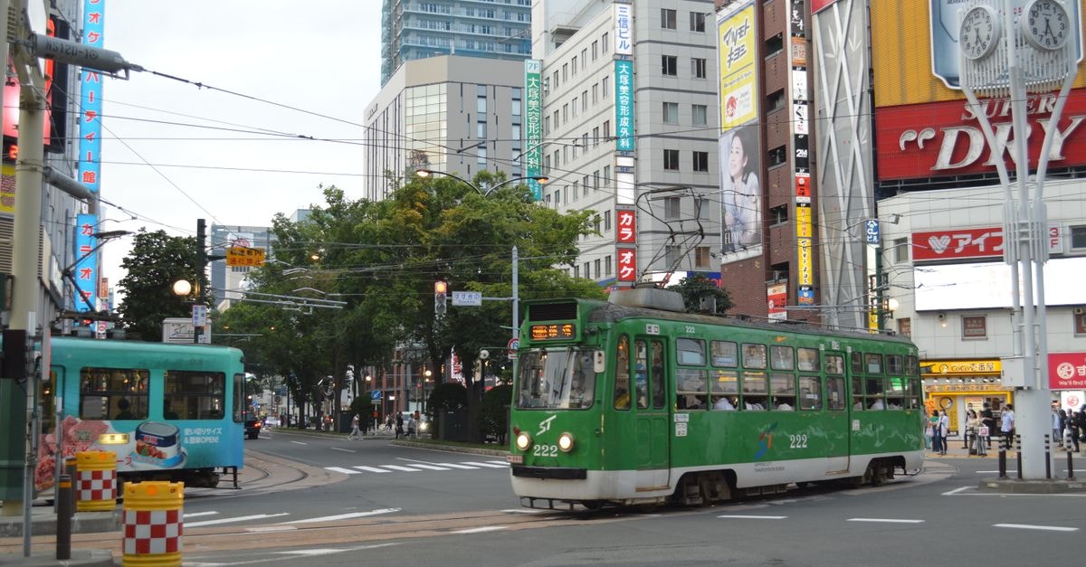 CROSS HOTEL SAPPORO in Sapporo: Susukino-Adjacent Stay with City Views Vibrant scene of a green tram navigating through a busy urban intersection in daylight.