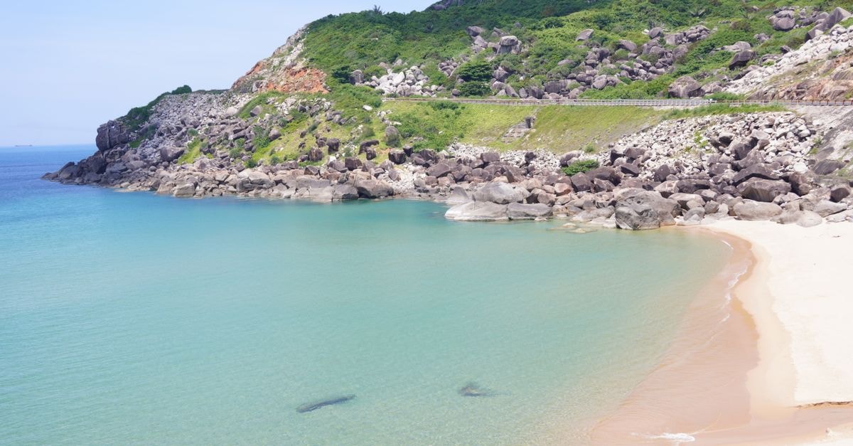 Cao Lanh Travel Guide: Planning Tips, Costs and Things to Do Idyllic beach cove with clear turquoise waters and rugged cliffs on a sunny day.