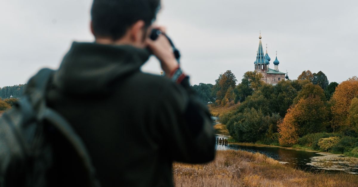 Back view of a tourist capturing a picturesque orthodox church surrounded by autumn foliage.