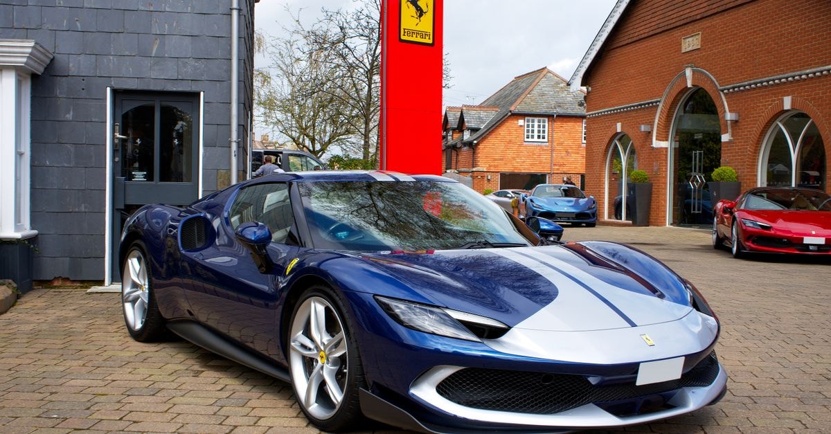 Jordan Brand Confirms Air Jordan 14 "Blue Ferrari" for Fall 2027 at $215 A sleek blue Ferrari supercar parked outside a dealership in an urban area.