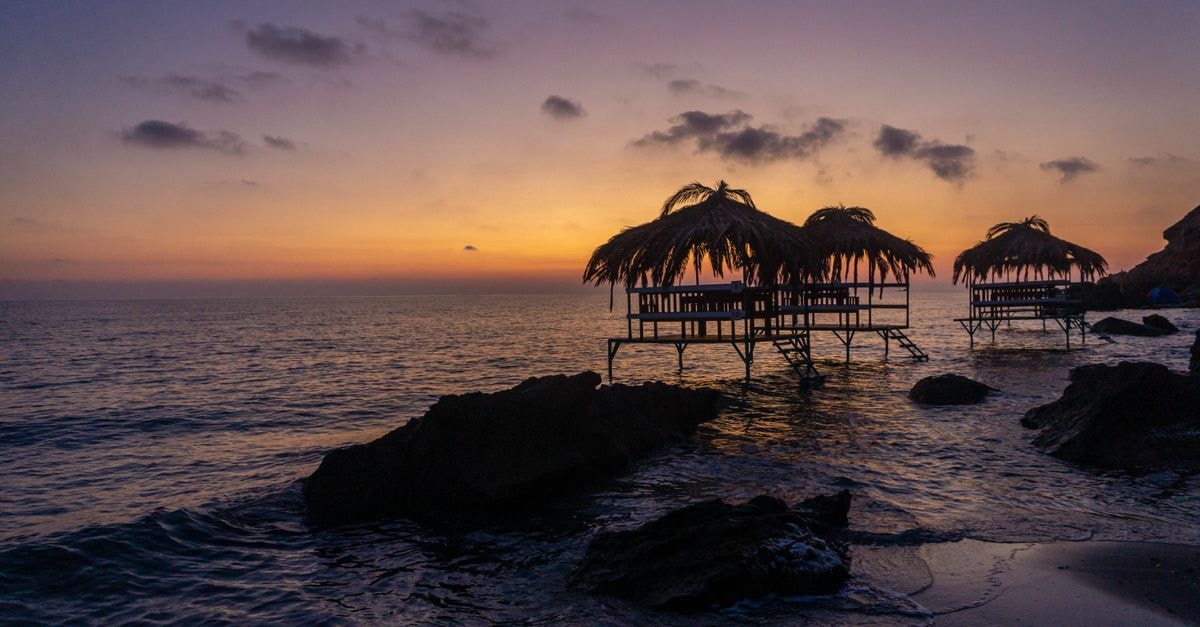 Scenic view of beach huts silhouetted against a stunning sunset over the ocean.