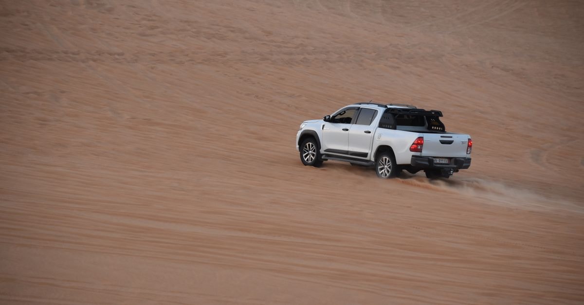 Gourara Hotel in Timimoun: A Pouillon Oasis Retreat A white truck speeding across the sandy dunes of Timimoun, Algeria in the desert.