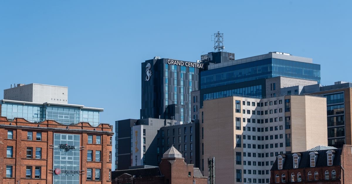 A daylight view of Belfast's urban skyline highlighting the Grand Central Hotel against a clear blue sky.