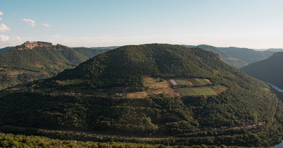 Volta Redonda Travel Guide: Planning Tips and Things to Do A stunning aerial view of lush green mountains with farmlands and a flowing river, perfect for nature lovers.