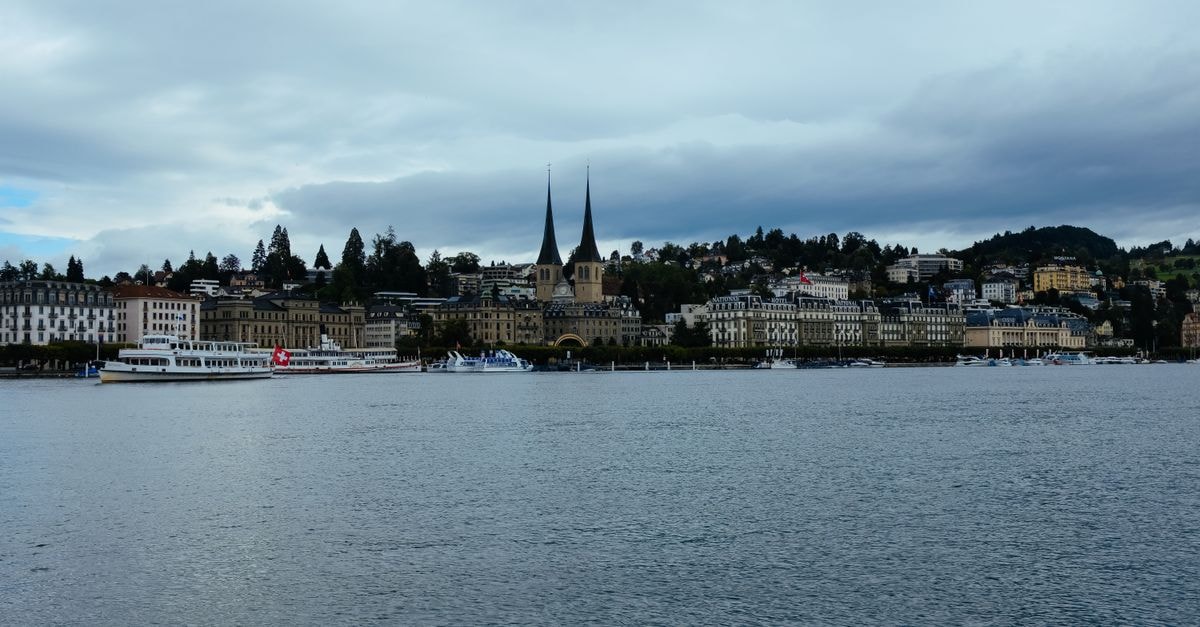 Capsule Hotel Lucerne, Lucerne — A Compact Pod Stay in Central Lucerne Picturesque waterfront view of Lucerne with iconic twin towers and overcast weather.