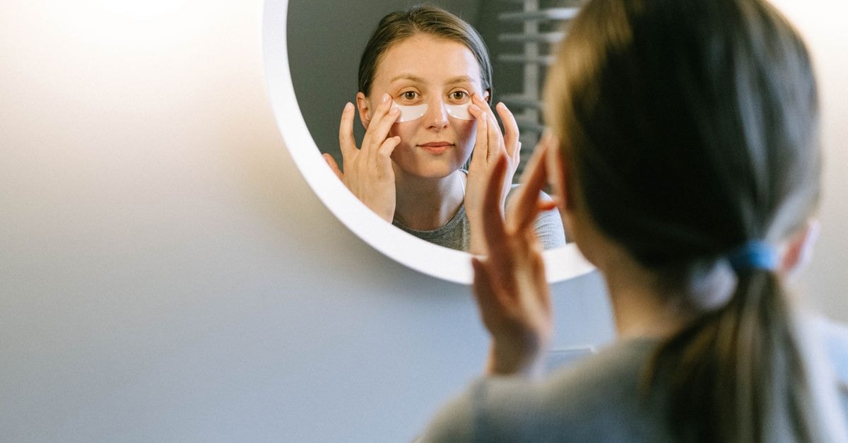 SpaceX's first post-IPO earnings put Musk's AI spending under Wall Street microscope A woman applying under-eye patches while looking in a round wall mirror, focusing on skincare.