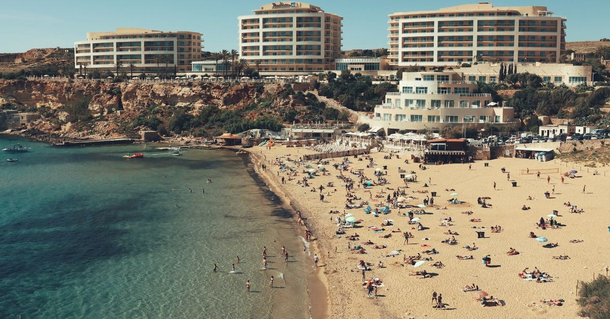 Marsaskala Travel Guide: A Relaxed Malta Coastal Escape A vibrant scene on Malta's sandy beach with tourists enjoying the sun and the Mediterranean Sea.