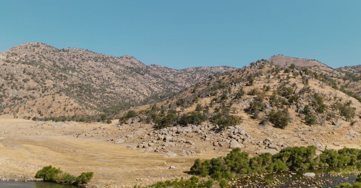 Arid landscape featuring rolling hills and sparse vegetation under a clear sky.