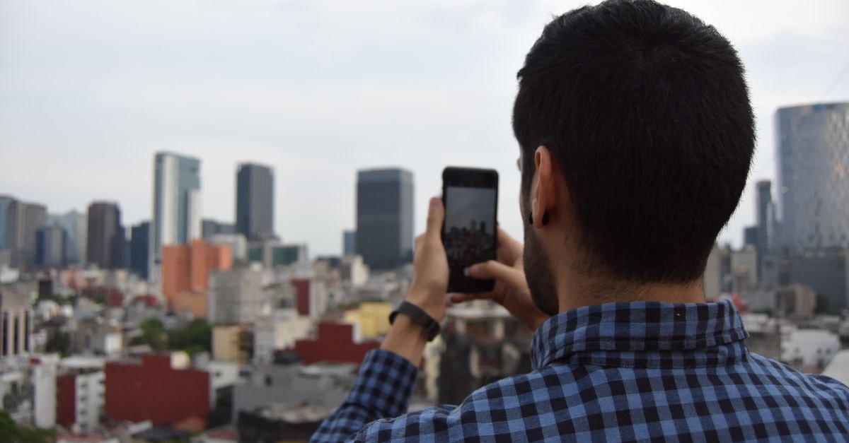Hotel & Villas Atizapan in Tlalnepantla: A New Vision of Comfort Man photographing urban cityscape with smartphone against skyline.