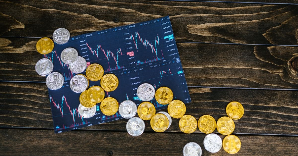 Gold rebounds from sub-$4,000 dip as split Fed holds rates steady Gold and silver cryptocurrency coins scattered on a trading chart over a wooden table.