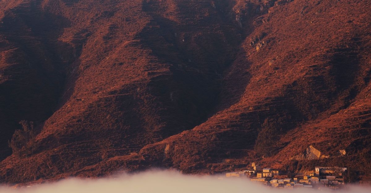 Dramatic sunset over a mist-shrouded village nestled in rugged mountain terrain.