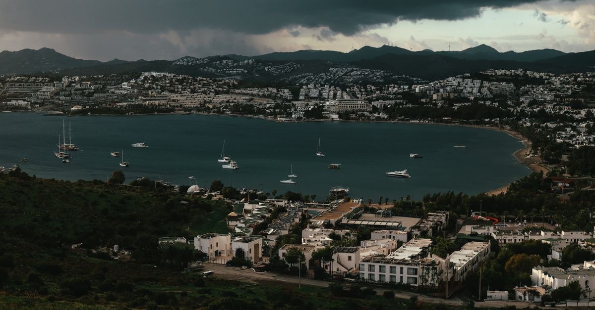 Dramatic aerial shot of a coastal city with boats and dark clouds overhead.
