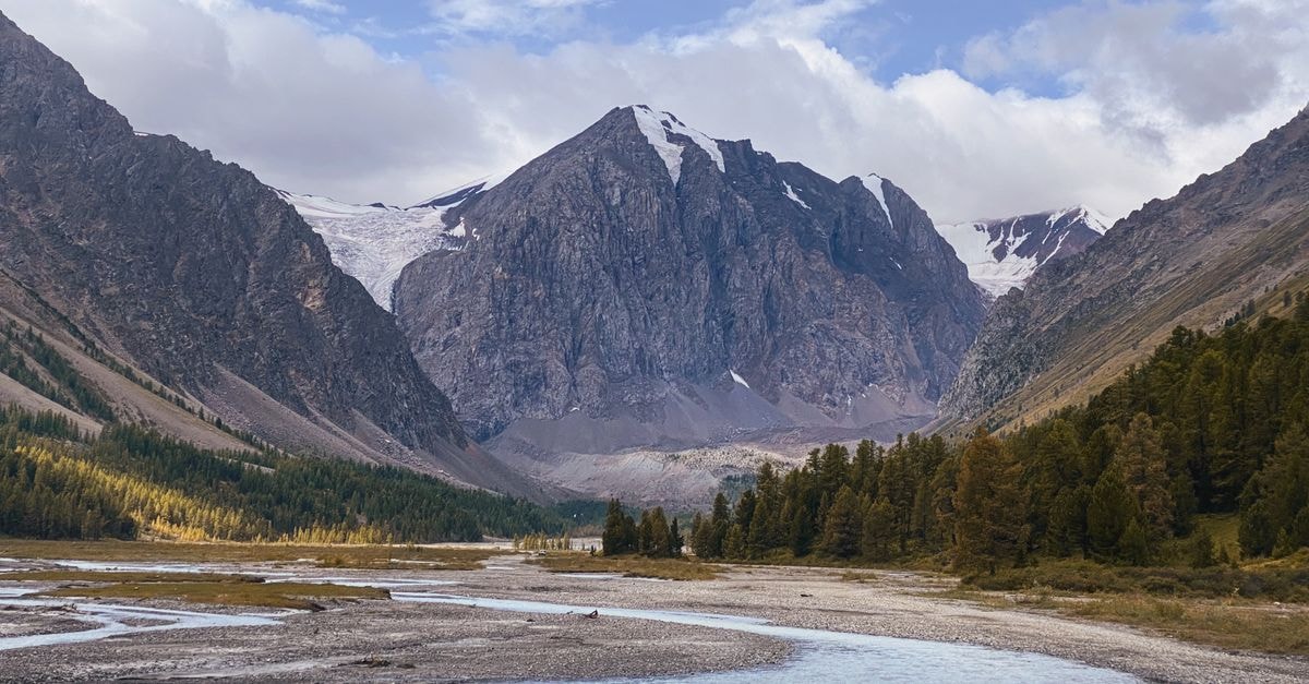 Breathtaking view of snow-capped mountains and river in Altai, Russia, showcasing untouched wilderness.