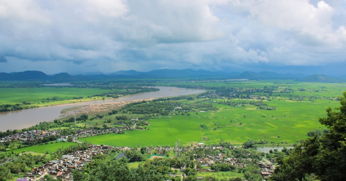 Aerial view capturing a vibrant green countryside landscape with a winding river and distant mountains.