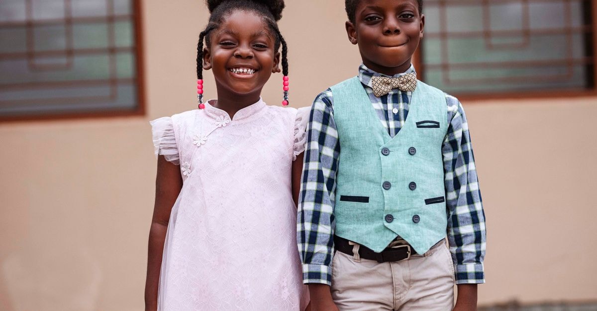 Adorable portrait of two smiling children in stylish outfits, outdoors in Accra, Ghana.