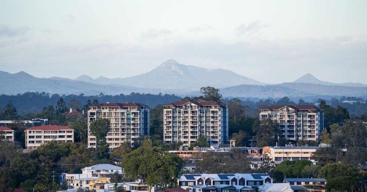 Logan City Travel Guide: Planning Tips, Costs and Things to Do Cityscape view of Brisbane, Australia with high-rise buildings and distant mountains under a clear sky.