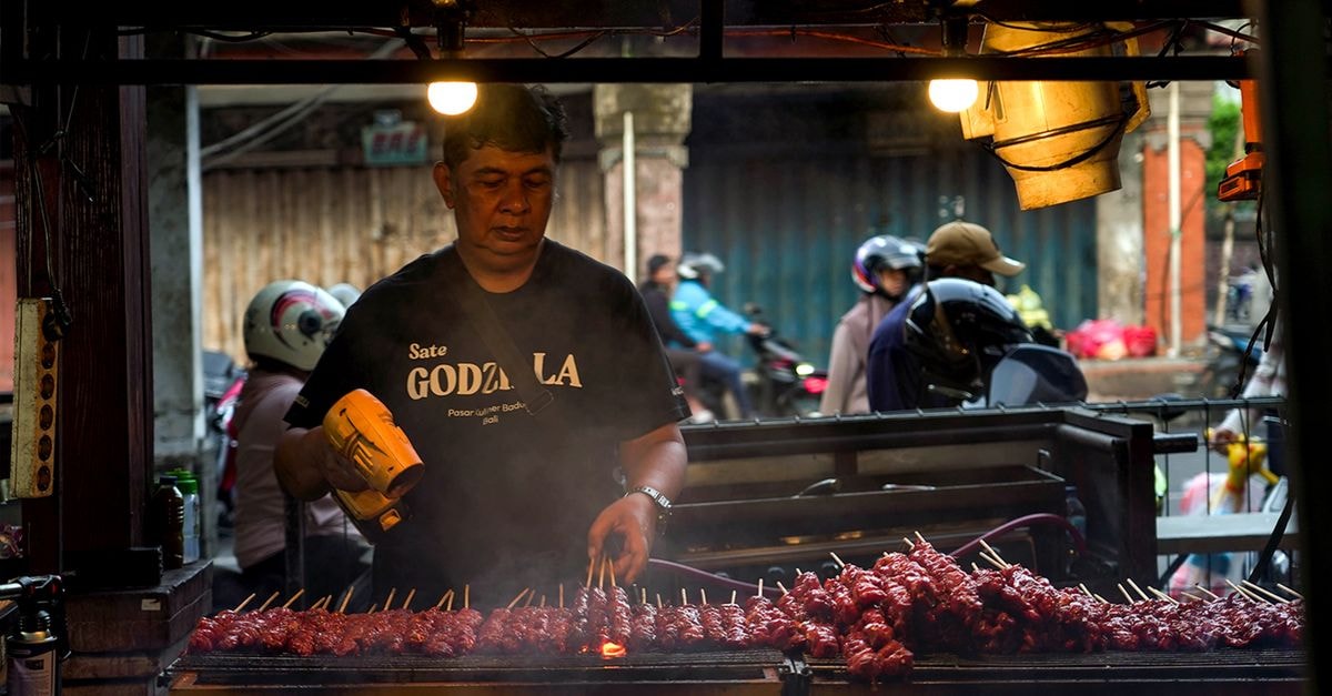 Grilling chicken satay at a street food market in Denpasar, Bali.