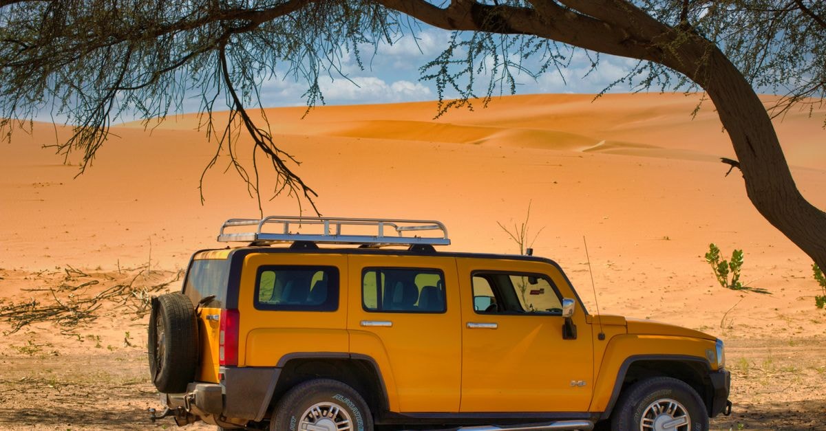 Zouérat travel guide: into Mauritania's iron heart by rail and 4x4 A yellow SUV parked in a vast desert landscape, shaded by a large tree, offering a scenic view.