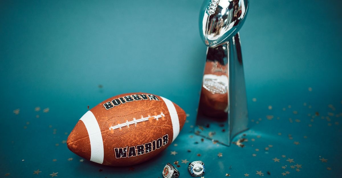 NFL Announces Jay-Z to Headline Super Bowl LXI Halftime Show Football and trophy with championship rings on a celebratory background.