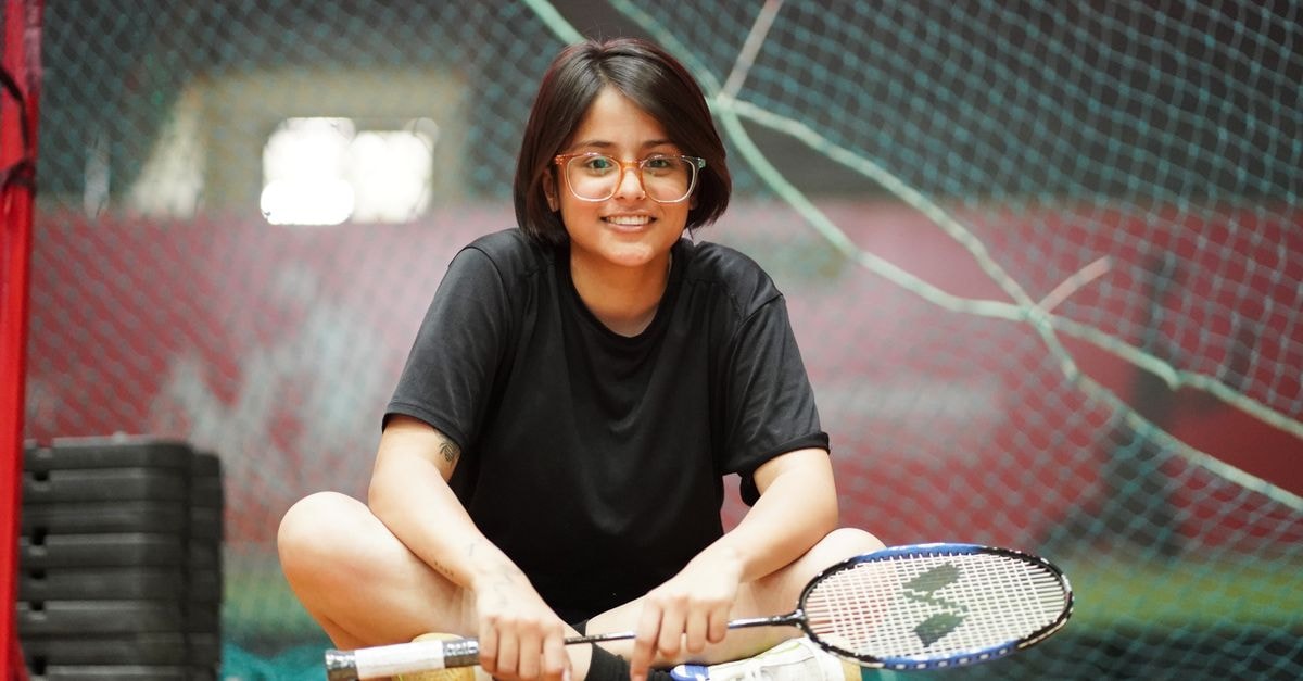 Tanvi Sharma reaches Taipei Open Super 300 final with straight-games win over Huang Yu-Hsun Smiling young woman seated on a court holding a badminton racket indoors, ready for a game.