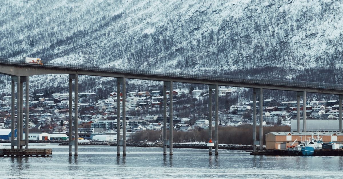 Scenic view of Tromsø Bridge with snowy mountains and calm waters, capturing winter in northern Norway.
