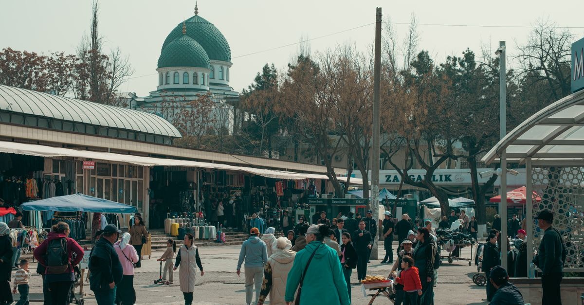 Tashkent Travel Guide: Planning Tips, Costs and Things to Do A bustling marketplace scene featuring diverse people and a mosque in the background in Uzbekistan.