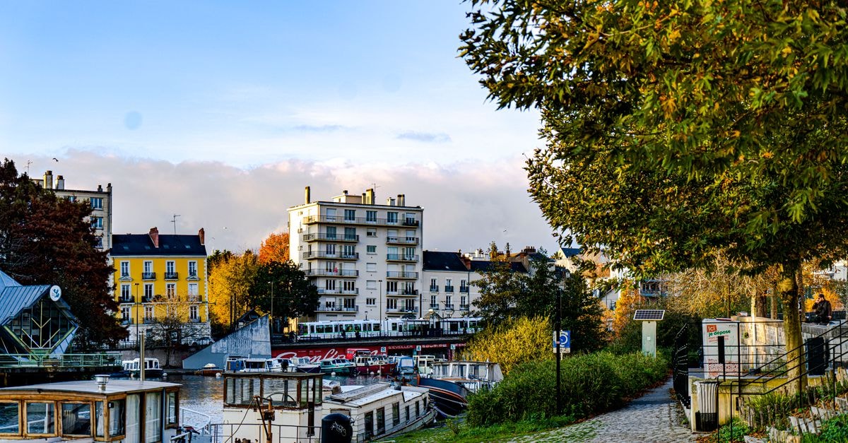 Nantes travel guide: gardens, riverside heritage and Loire-edge flavors Charming riverside view of Nantes, France, showcasing boats, buildings, and autumn scenery.