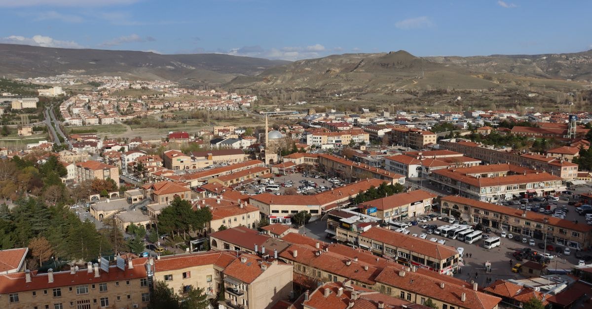 Aerial view of a picturesque town in Cappadocia, Turkey, showcasing red rooftops and surrounding hills under a clear sky.