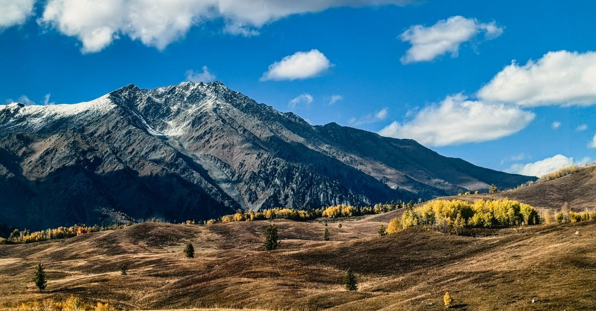 An Altay Travel Guide for Slow Travelers Who Love Wild Horizons A breathtaking view of snow-capped mountains surrounded by autumn foliage under a clear blue sky.