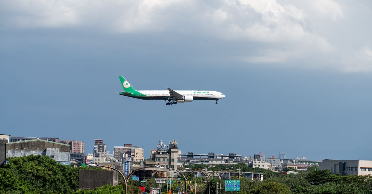 Airplane descends over urban landscape on a clear day with scattered clouds.