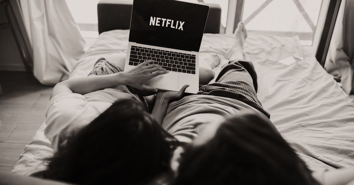 A couple relaxing together, watching Netflix on a laptop in a cozy bedroom setting.