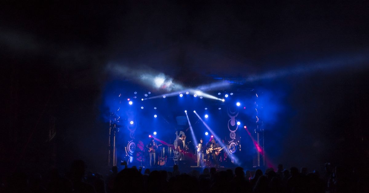 High-energy band performance on a stage with colorful lights and an engaged crowd.
