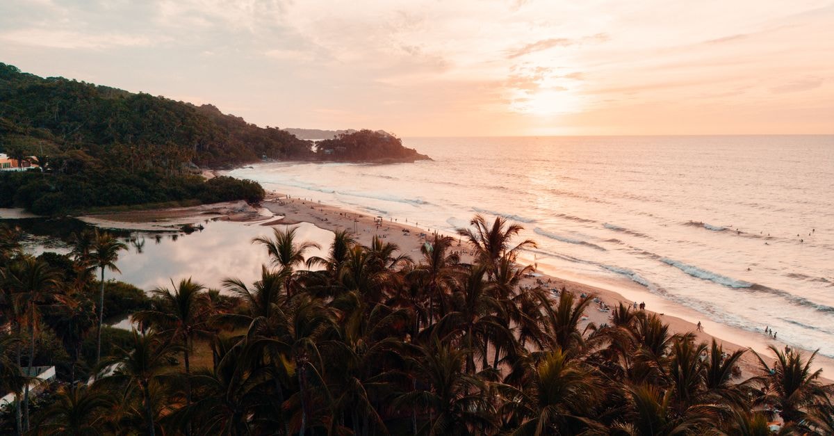Salsa, Sunsets, and Slow Mornings: A Travel Guide to Cali Aerial view of a serene tropical beach at sunset with palm trees and calm waves in San Francisco, Nayarit, México.