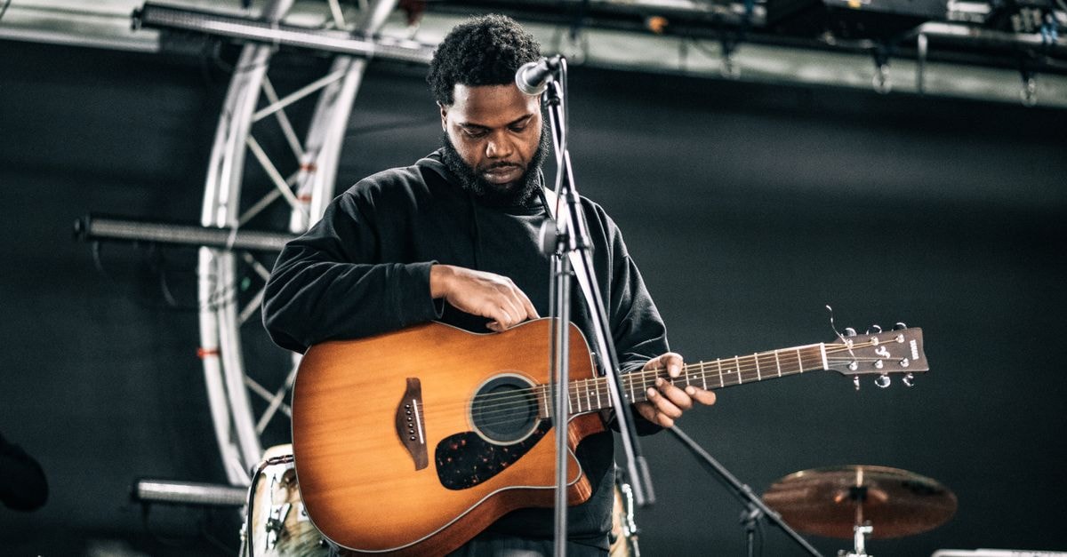 A male musician tuning his guitar on stage before a live performance.