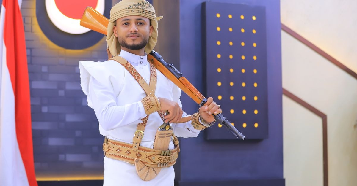 A man in traditional Yemeni dress poses with a rifle indoors in Sana'a, Yemen.