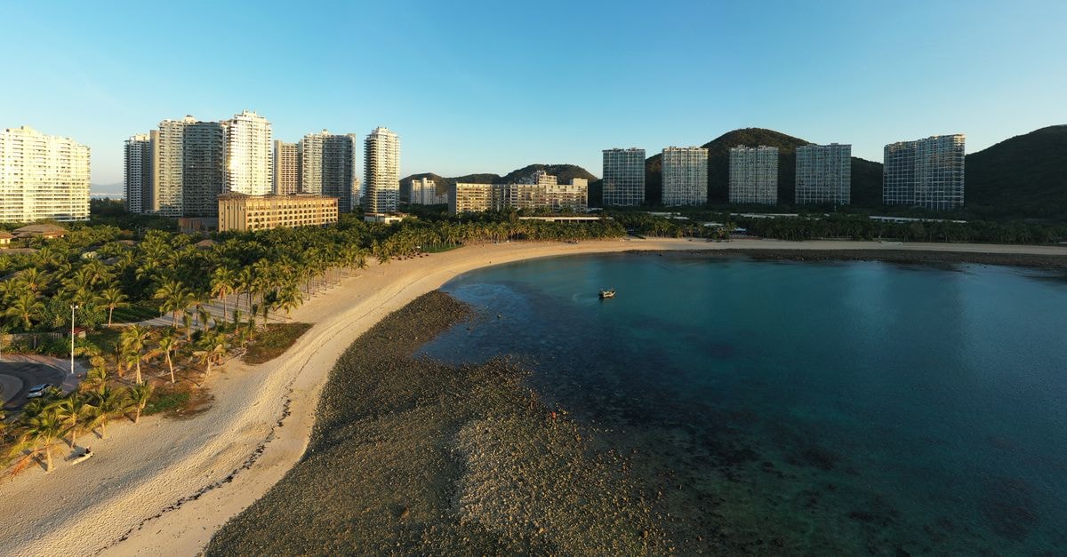 Sanya Travel Guide: Tropical City Moves and Local Flavor Aerial view of Sanya's beachfront with city skyline, palm trees, and clear water.