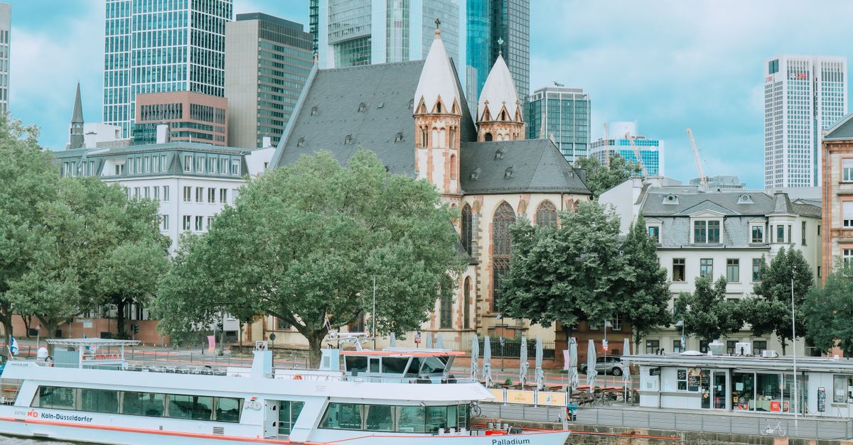 Frankfurt cityscape featuring a historic church, modern skyscrapers, and a boat along the river.