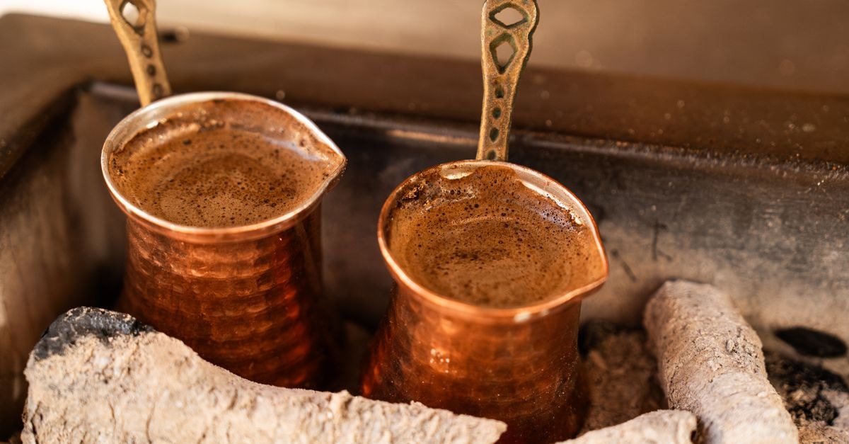 Two copper pots brewing coffee over hot coals, evoking traditional Turkish coffee culture.