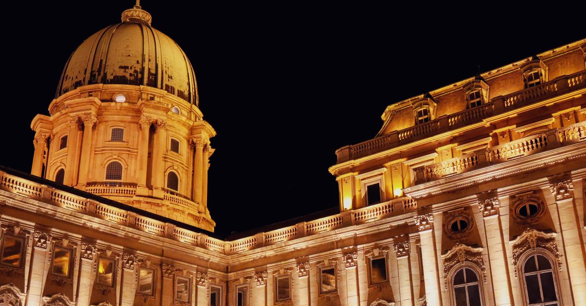 Illuminated Buda Castle dome and facade at night in Budapest, Hungary, showcasing Baroque architecture.