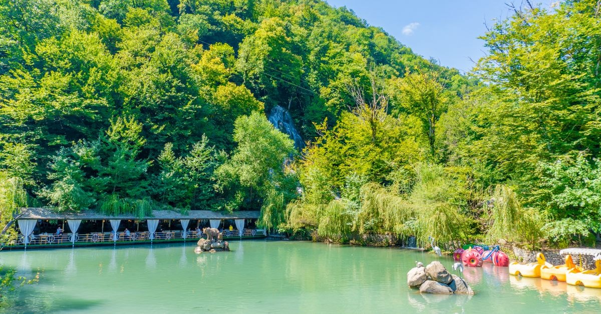 Dosso Travel Guide: Planning Tips, Costs and Things to Do Tranquil lakeside view with lush green forest and pedal boats, perfect for summer leisure.