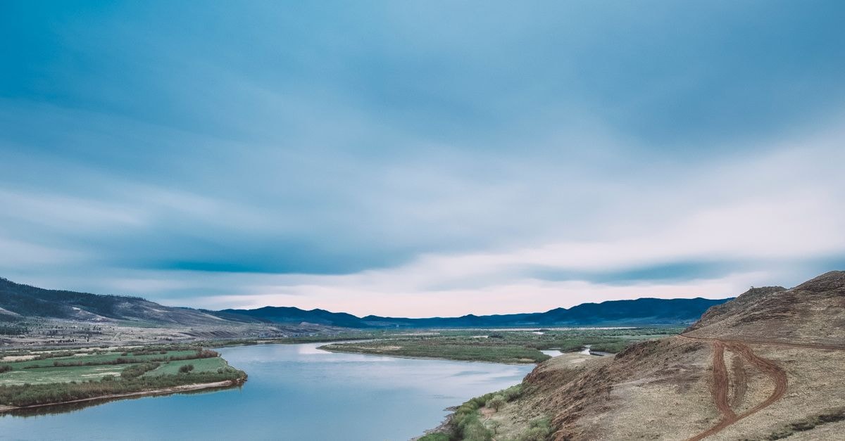 Kamloops Travel Guide: Planning Tips, Costs and Things to Do Scenic view of a tranquil river winding through lush hills under a vibrant blue sky.