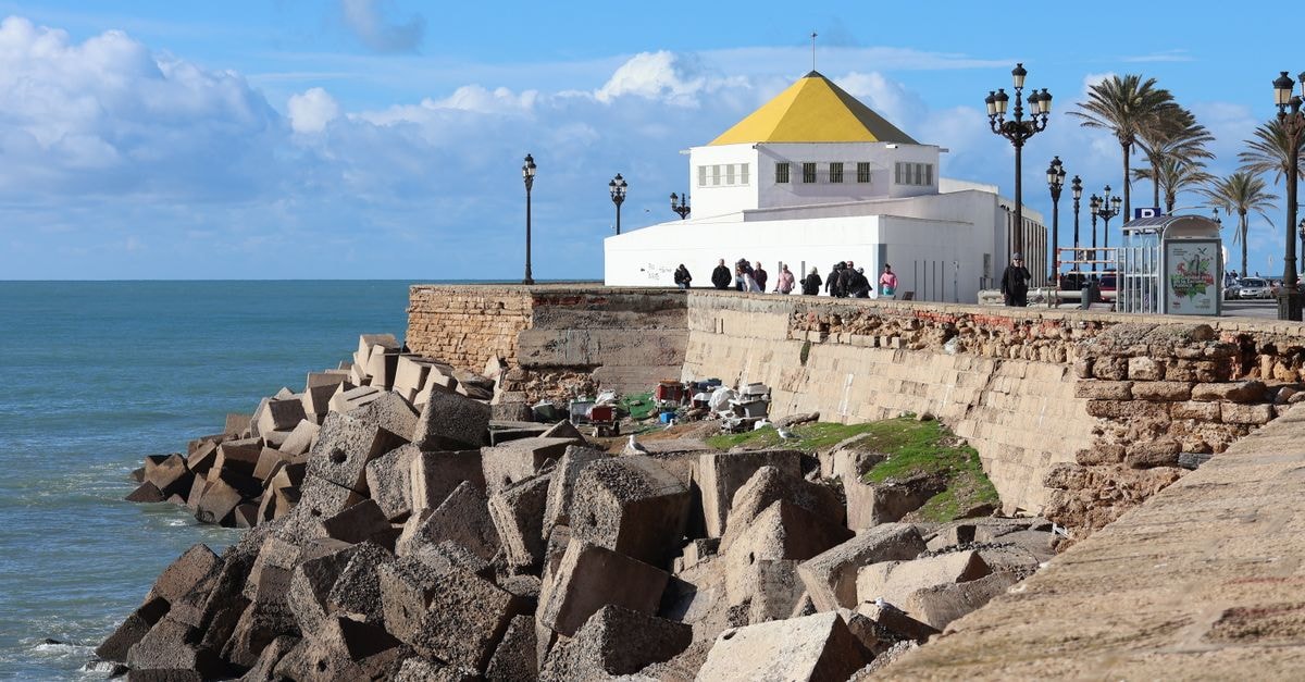Bafoussam Travel Guide: Planning Tips, Costs and Things to Do View of a coastal promenade in Cádiz, Andalucía, with rocky shoreline and bright blue sky.