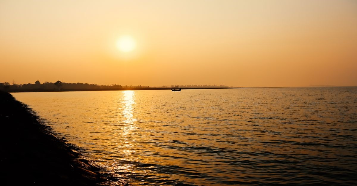 Kakinada Travel Guide: A Quiet Coastal City Worth a Slow Stop Beautiful sunset over a tranquil body of water in Sambalpuri, India, capturing a serene boating silhouette.